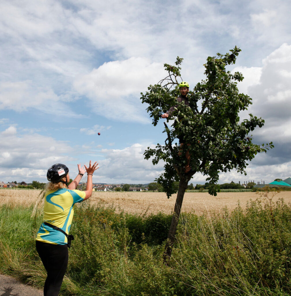 MUT-TOUR_Unterstützung_Sucht_Depression Ein MUT-TOUR-Teilnehmer sitzt in einem Baum und wirft Michaela etwas zu