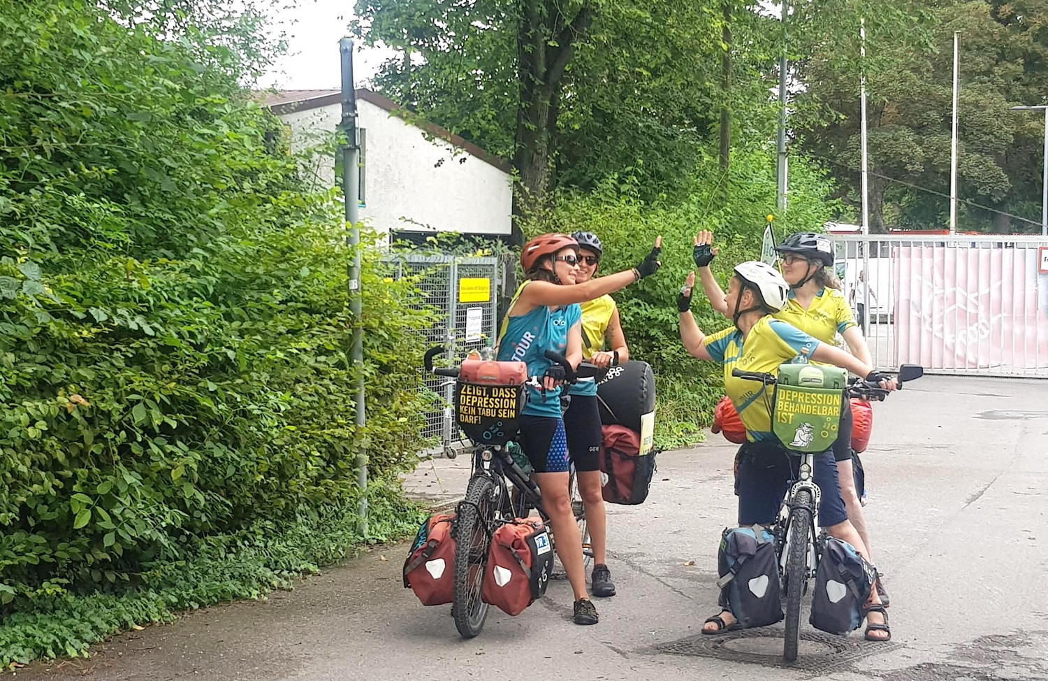 Vier MUT-TOUR-Teilnehmende auf zwei Tandems, die nebeneinander stehen und sich abklatschen