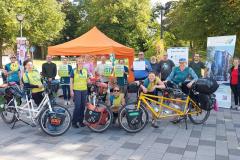 Mehrere Menschen mit Tandem und Schildern vor einem Stand bei einem MUT-TOUR Aktionstag.