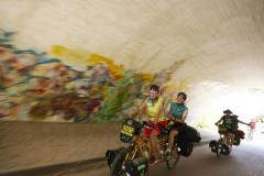 MUT-TOUR-Teilnehmende auf Tandems fahren durch einen mit Graffiti besprühten Tunnel. (c) Sebastian Arlt