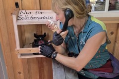 Eine MUT-TOUR-Teilnehmerin mit einem Eis in der Hand telefoniert mit einem alten Apparat, daneben ein Schild mit "Nur für Selbstgespräche"