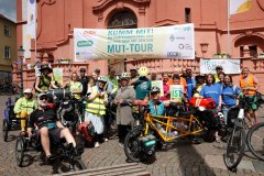 Teilnehmende einer Mitfahr-Aktion der MUT-TOUR 2026 mit Rädern, Tandems und großem Banner (c) Sebastian-Burger